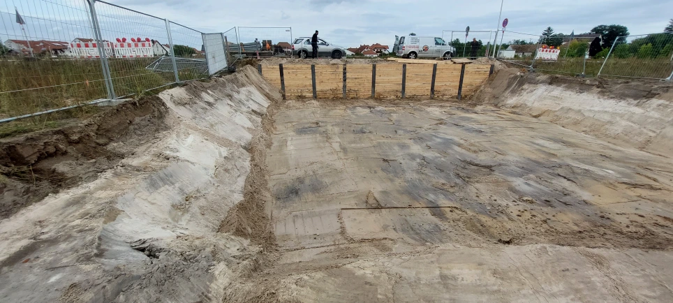 Ausgehobene Baugrube mit ebener Sohle, seitlichen Böschungen und Holzverbau am hinteren Rand