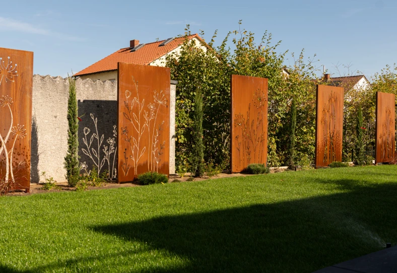 Dekorative Metallelemente mit Pflanzenmotiven entlang des Rasens