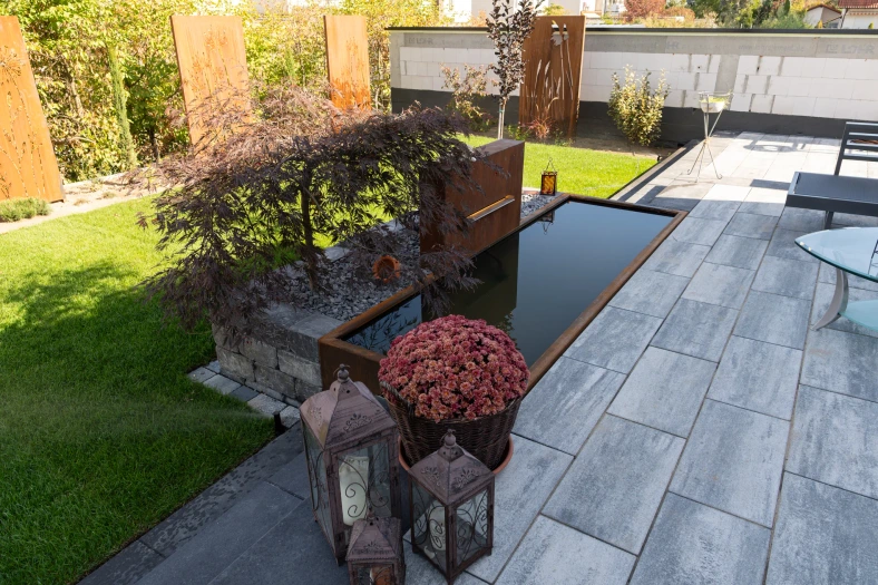 Großformatige Terrassenplatten neben dem Gartenbrunnen und bepflanztem Hochbeet