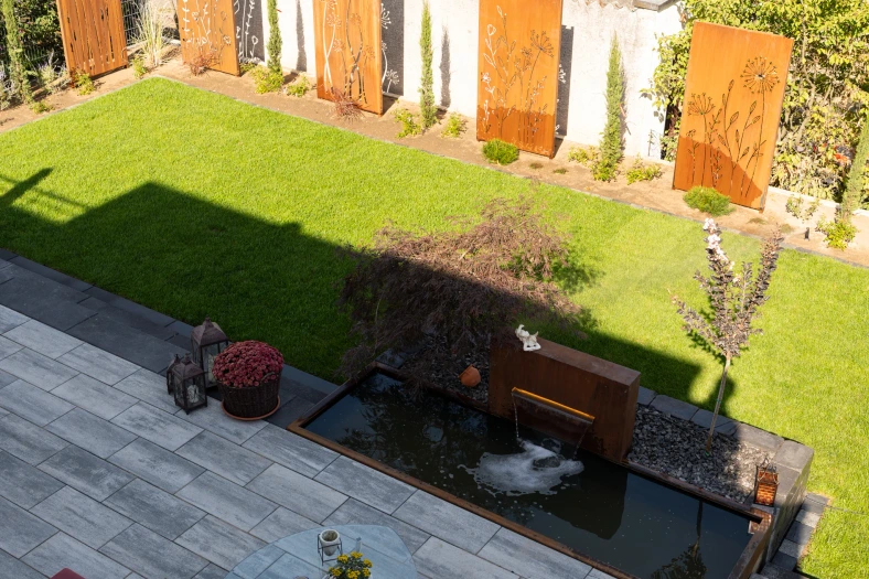 Blick von oben auf Terrassenplatten, Gartenbrunnen und Rasen