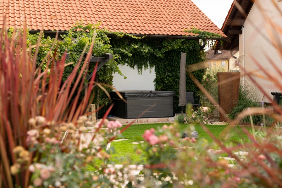 Blick durch Gräser und blühende Pflanzen auf den überdachten Gartenbereich