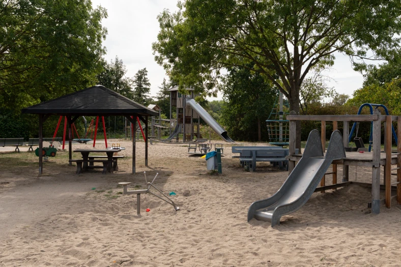 Rutschen und Klettergeräte auf dem benachbarten Spielplatz unter großen Bäumen in Erpolzheim