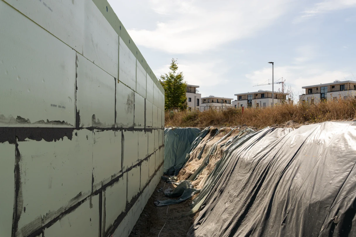 Offener Arbeitsraum zwischen gedämmter Kelleraußenwand und folienbedeckter Baugrubenböschung