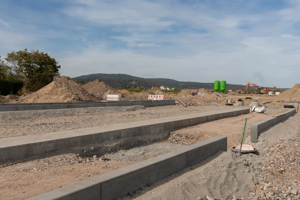 Vorbereitete Straßenflächen mit Bordsteinen, Erdlagern und einem Bagger im Neubaugebiet Am Schwabenbach in Wachenheim
