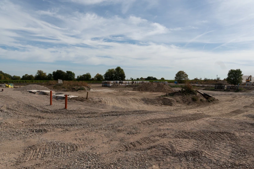 Weite Ansicht des Neubaugebiets mit Baustraße, Schotterflächen und angrenzenden Weinbergen